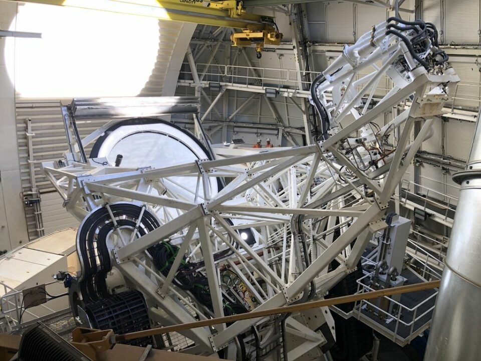 Telescope_Mount_Assembly_of_the_Inouye_Solar_Telescope En stor vit teleskopkonstruktion med fackverksram, kablar och mekaniska komponenter står inne i en observatoriebyggnad. Runt konstruktionen syns gångplattformar, räcken och lyftutrustning.