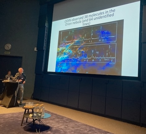 Aage Sandqvist shows one of the astronomical discoveries made by Odin during the event_Bengt Larsson-SU Department of Astronomy En talare står framför en stor skärm som visar en vetenskaplig presentation om ODIN-observationer av molekyler och spektrallinjer i Orionnebulosan.
