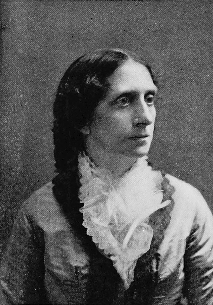 Angeline_Stickney_public domain Ett svartvitt porträtt av en kvinna med mörkt hår benat på mitten, klädd i en vit spetsblus med hög krage och volanger, under en mörk jacka.