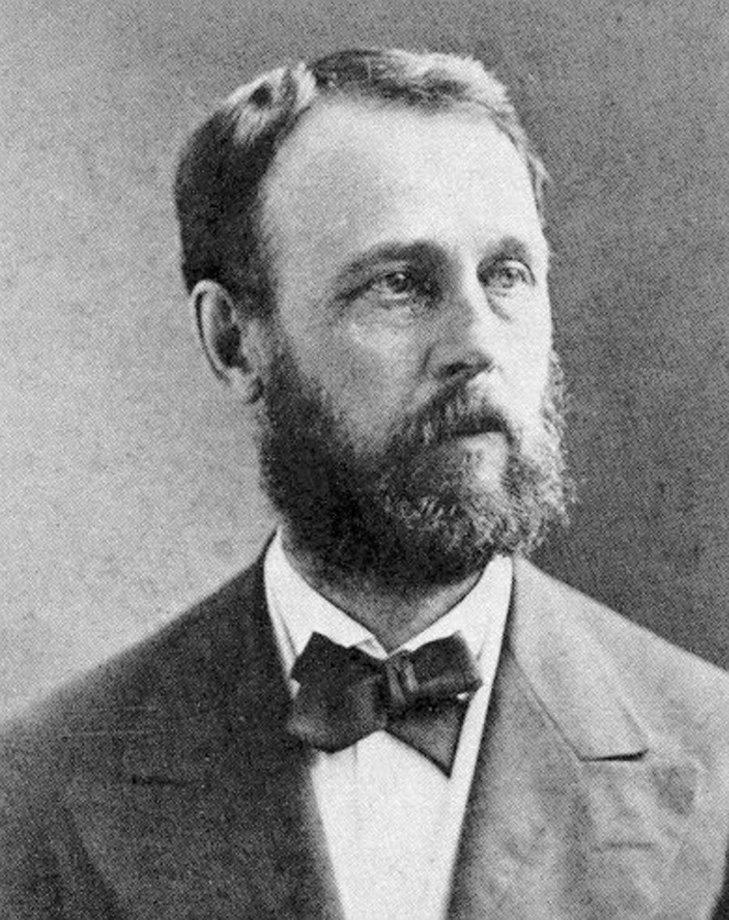 Asaph-Hall_public domain Ett svartvitt porträtt av en man med ett fylligt skägg, klädd i kavaj, vit skjorta med krage och en mörk fluga, blickande åt höger.