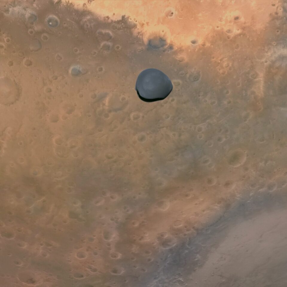 Deimos_Over_Mars,_Terra_Sabaea_-_ESA_Hera_Mission Månen Deimos syns 300 km ovanför Mars kraftigt kraterfyllda, roströda yta och skapar en stark, ensam fokuspunkt i mitten