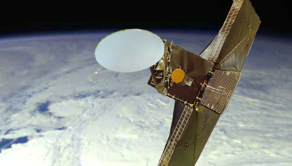 Odin_SSC Space En satellit med en stor, cirkulär antenn och mörka solpaneler kretsar ovanför jorden, som syns nedanför som ett suddigt halvt klot med vita moln.