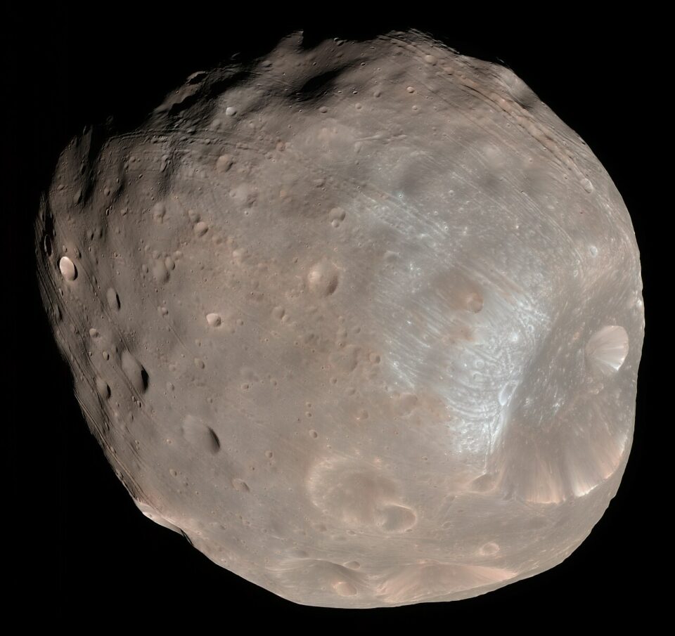 En högupplöst bild av månen Phobos mot en svart bakgrund, som visar dess kraterfyllda, grå och oregelbundna yta samt tydliga linjära fåror.