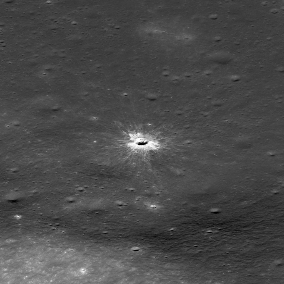 Oblique view of McGetchin crater from LRO_NASA-GSFC-Intuitive Machines En svartvit flygbild av månens yta som visar en liten, ljusstark nedslagskrater omgiven av ett strålande mönster av ljusfärgat utkastat material.